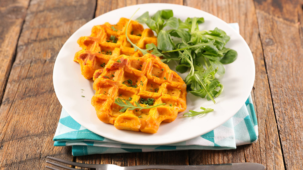 Zwei Süßkartoffel-Waffeln liegen neben Salat auf einem Teller.