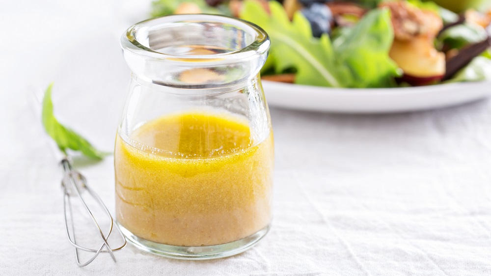 Vinaigrette in einem Glas, im Hintergrund Salat.