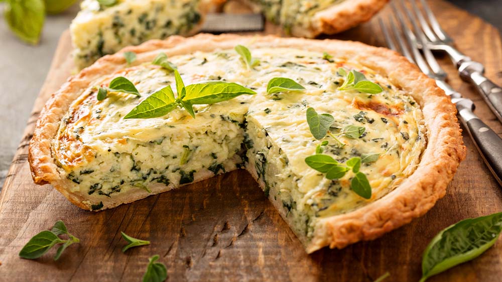 Quiche mit Kräutern und Spinat auf Holzbrett