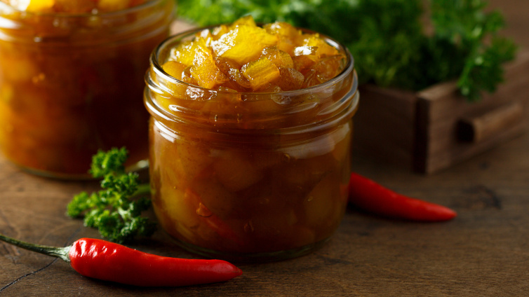 Mango-Chutney in zwei Gläsern neben Chilischoten und Kräutern.