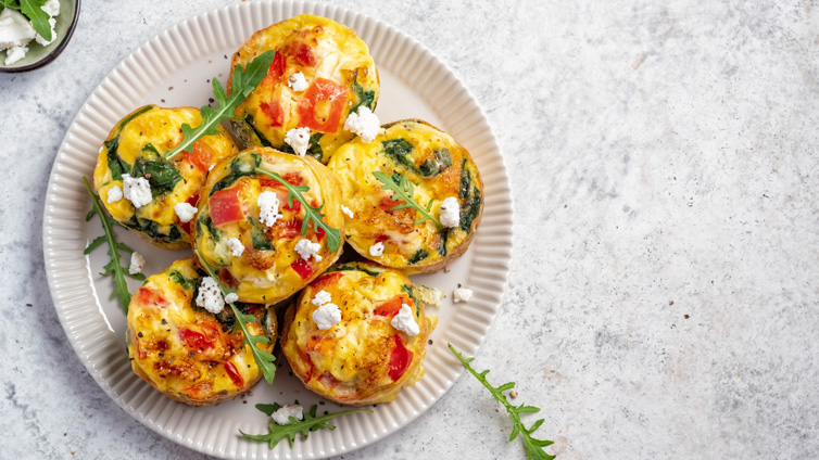 Sechs Egg Muffins mit Feta und Rucola liegen auf einem Teller.