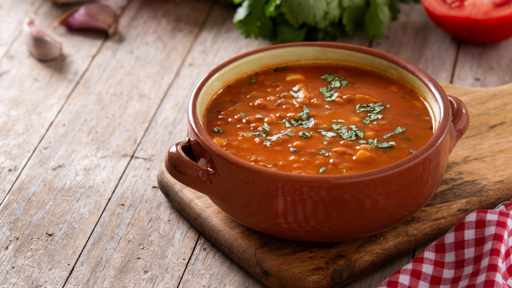 Rote Linsensuppe in Schüssel auf einem Holzbrett.