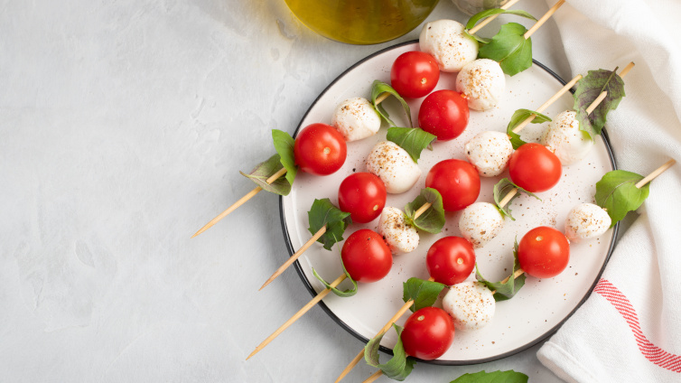 Tomate-Mozzarella-Spieße mit Basilikum liegen auf einem Teller.